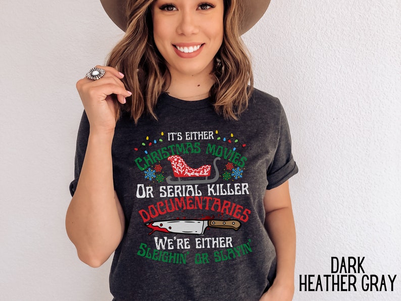 May include: Dark heather gray t-shirt with a Christmas and serial killer themed graphic. The graphic features a red sleigh with a Christmas tree and the text "It's either Christmas movies or serial killer documentaries. We're either sleighin' or slayin'."
