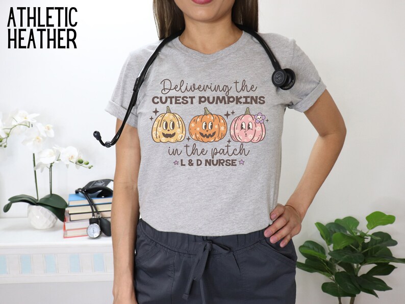 May include: Athletic heather gray t-shirt with the text "Delivering the cutest pumpkins in the patch L&D Nurse" and three cartoon pumpkins. The shirt is worn with gray scrubs and a stethoscope.