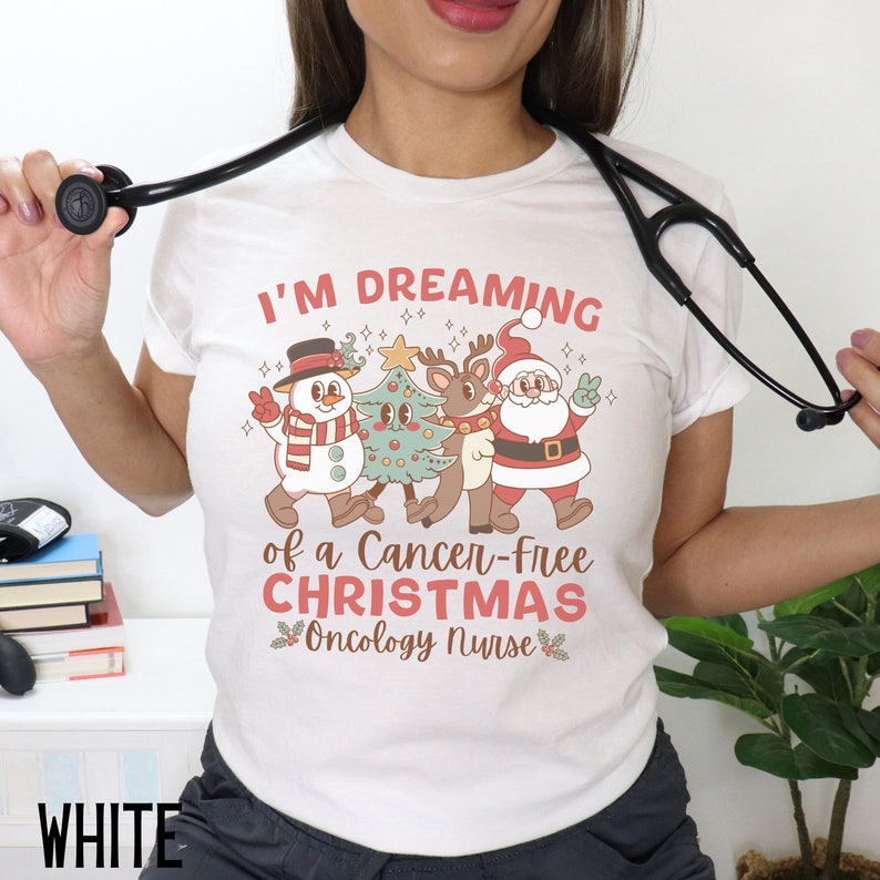 May include: White t-shirt with a Christmas-themed design featuring a snowman, reindeer, and Santa Claus. The text reads "I'm Dreaming of a Cancer-Free Christmas Oncology Nurse".
