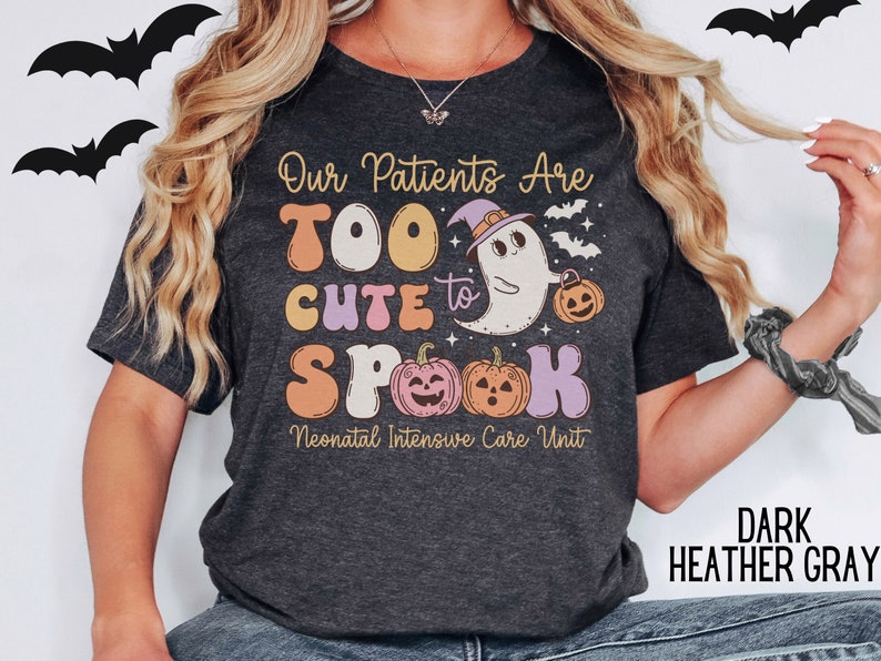 May include: Dark heather gray t-shirt with a cute ghost wearing a witch hat and holding a pumpkin. The text on the shirt reads "Our Patients Are Too Cute to Spook Neonatal Intensive Care Unit".