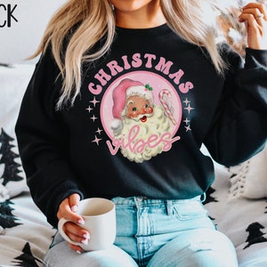 May include: Black sweatshirt with a pink and white graphic of a cartoon Santa Claus with the text "Christmas Vibes".