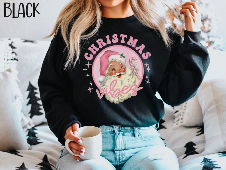 May include: Black sweatshirt with a pink and white graphic of a cartoon Santa Claus with the text "Christmas Vibes".