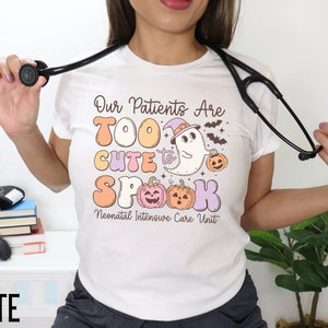 May include: White t-shirt with a Halloween-themed design that says "Our Patients Are Too Cute To Spook" with a ghost and pumpkins. The text "Neonatal Intensive Care Unit" is below the design.