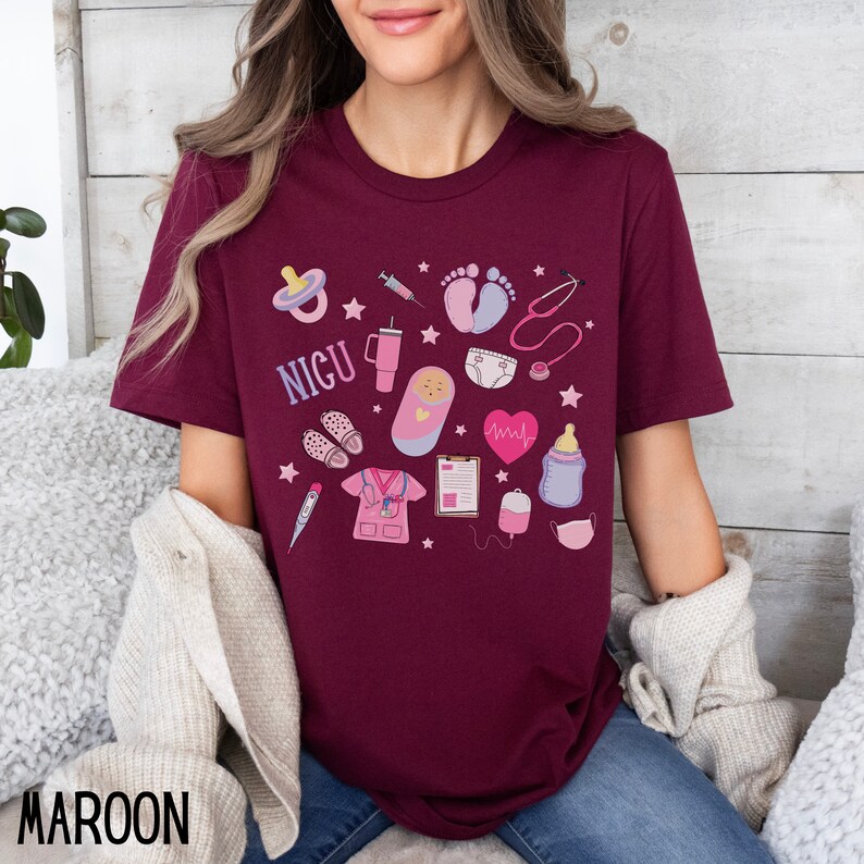 Puede incluir: Una camiseta color burdeos con un dise&ntilde;o gr&aacute;fico de varios s&iacute;mbolos m&eacute;dicos y la palabra "NICU". Los s&iacute;mbolos incluyen un estetoscopio, un biber&oacute;n, un chupete, una jeringa, un term&oacute;metro, un monitor de frecuencia card&iacute;aca, una huella de pie de beb&eacute;, un pa&ntilde;al y un beb&eacute; en un arrullo.