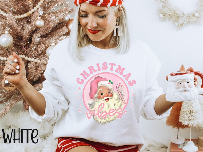 May include: White sweatshirt with a pink and white Christmas graphic featuring a cartoon Santa Claus with the text "Christmas Vibes".
