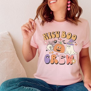 May include: A pink t-shirt with a retro-style graphic that says "NIGH BOO CREW" with a ghost, pumpkin, and spider web design.