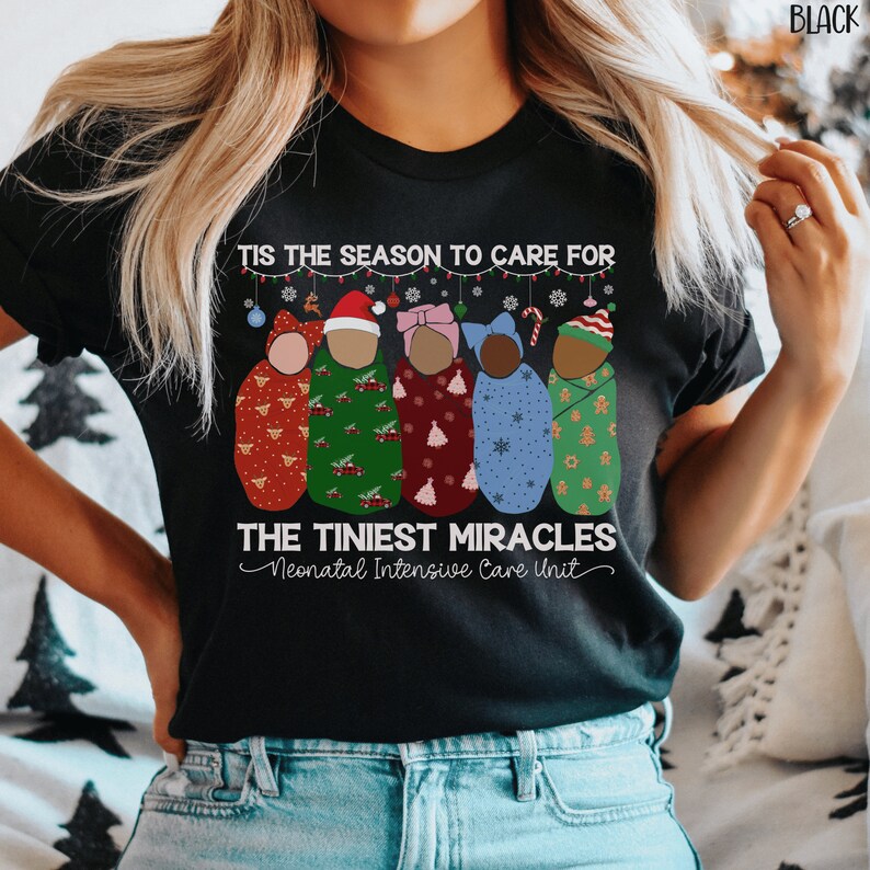 K&ouml;nnte beinhalten: Schwarzes T-Shirt mit einem weihnachtlichen Design mit f&uuml;nf Babys, die in Decken mit verschiedenen Weihnachtsmustern gewickelt sind. Der Text lautet "Tis the season to care for the tiniest miracles Neonatal Intensive Care Unit".