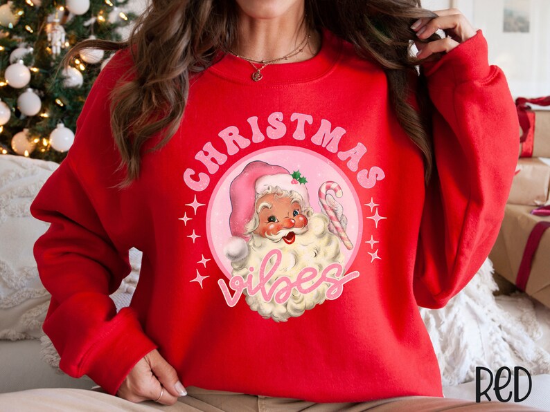 May include: Red Christmas sweatshirt with a pink circle graphic featuring a cartoon Santa Claus with the text "Christmas Vibes".