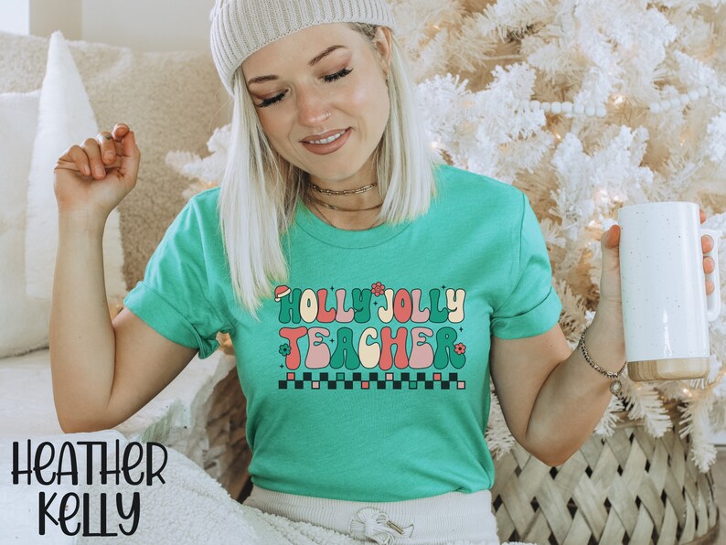 May include: A green t-shirt with the text "Holly Jolly Teacher" in a retro font with a red Santa hat, green holly leaves, and pink flowers. The text is in a colorful, wavy font.