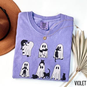 May include: A purple t-shirt with a graphic of black cats and ghosts. The text "Comfort Colors" is on the tag.