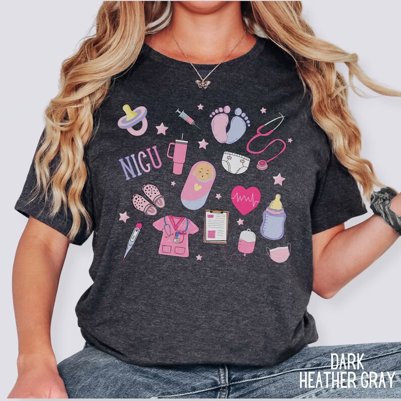 Puede incluir: Camiseta gris oscuro jaspeada con un dise&ntilde;o gr&aacute;fico de varios s&iacute;mbolos m&eacute;dicos y la palabra "NICU". El gr&aacute;fico incluye un estetoscopio, una jeringa, un biber&oacute;n, un chupete, una huella de pie de beb&eacute;, un monitor de frecuencia card&iacute;aca, un term&oacute;metro, un pa&ntilde;al para beb&eacute;, un beb&eacute; en un arrullo, un uniforme de enfermera, un portapapeles, una bolsa de sangre y una mascarilla facial.