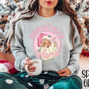 May include: A gray sweatshirt with a pink circle graphic featuring a vintage Santa Claus illustration and the text "Christmas Vibes".