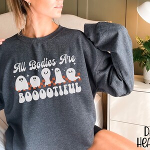 May include: A dark heather grey sweatshirt with a white graphic of ghosts and the text "All Bodies Are Boootiful".