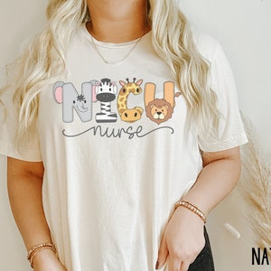 K&ouml;nnte beinhalten: Ein wei&szlig;es T-Shirt mit einer Grafik von Tieren, die "NICU nurse" buchstabieren. Die Tiere sind ein Zebra, eine Giraffe, ein Elefant und ein L&ouml;we.