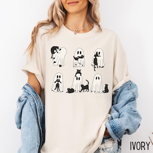 May include: A white t-shirt with a black and white graphic of ghosts and cats. The text "IVORY" is visible in the bottom right corner of the image.