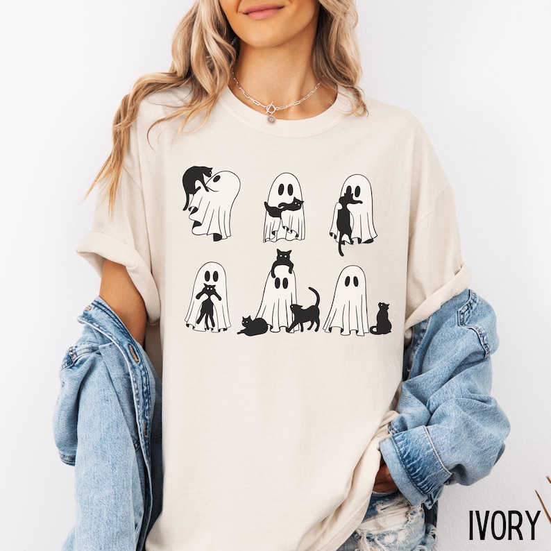 May include: A white t-shirt with a black and white graphic of ghosts and cats. The text "IVORY" is visible in the bottom right corner of the image.