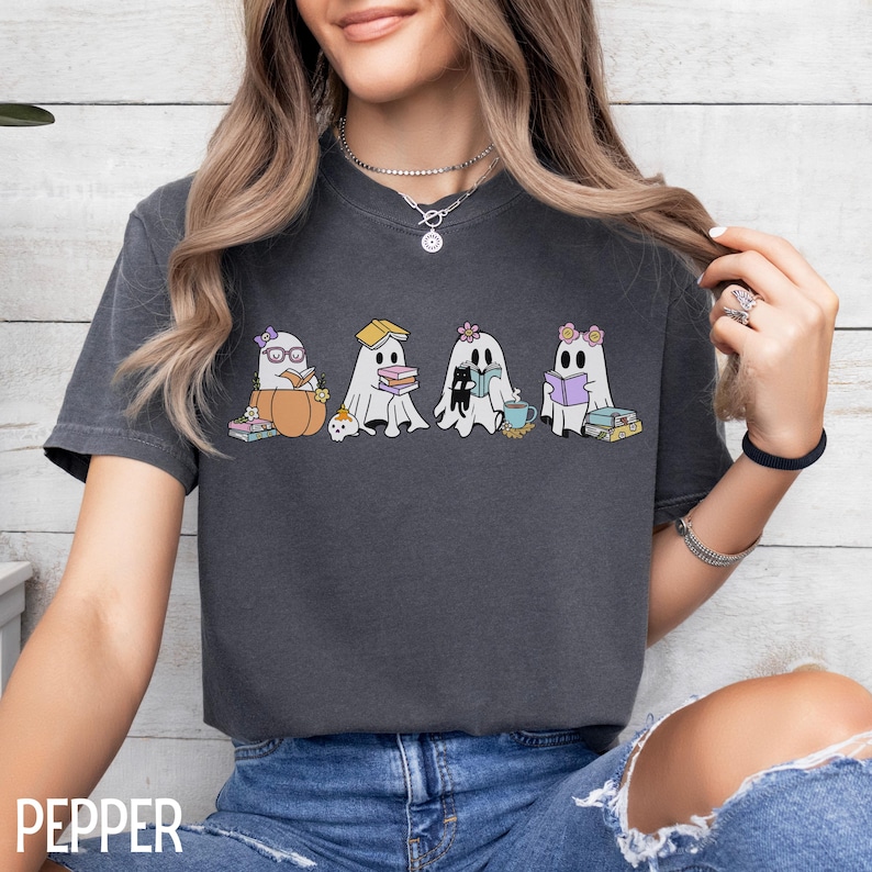 May include: Dark gray t-shirt featuring a graphic of four cartoon ghosts reading books. The ghosts are in a row, each with a unique accessory, such as glasses, a flower, and a teacup. The word "PEPPER" is printed at the bottom.