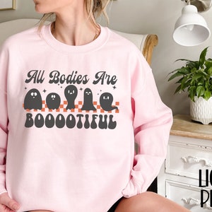 May include: A pink sweatshirt with the text "All Bodies Are Boo-ootiful" in black and orange. The text is surrounded by five black ghosts.