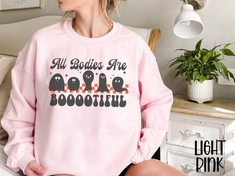 May include: A pink sweatshirt with the text "All Bodies Are Boo-ootiful" in black and orange. The text is surrounded by five black ghosts.