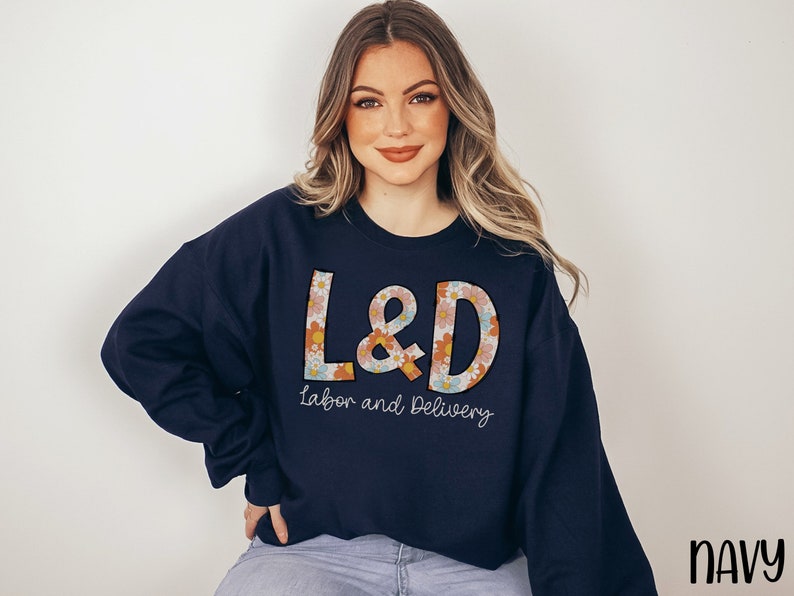May include: Navy blue sweatshirt with the letters "L&D" in a floral design, with the words "Labor and Delivery" underneath. The word "NAVY" is in the bottom right corner.