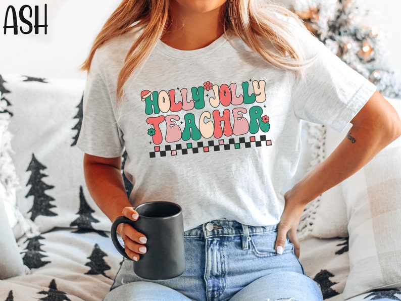 May include: A white t-shirt with the text "Holly Jolly Teacher" in a retro, colorful font. The text is surrounded by small red and green flowers and a black and white checkered pattern.