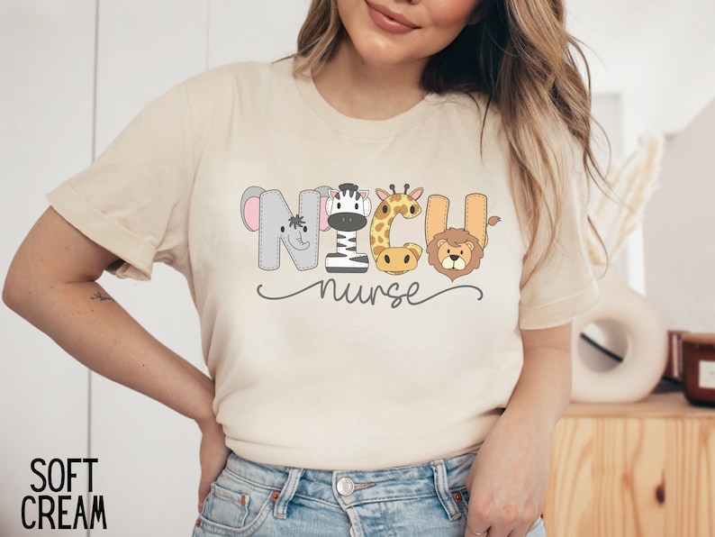 K&ouml;nnte beinhalten: Ein cremefarbenes T-Shirt mit einer Grafik aus Tierillustrationen, die "NICU nurse" buchstabieren.