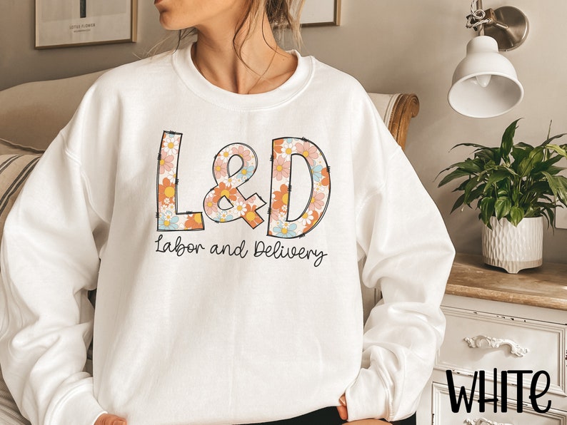 May include: White sweatshirt with the letters "L&D" in a floral design, with the words "Labor and Delivery" underneath. The sweatshirt is a crew neck style.