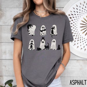 Puede incluir: Una camiseta gris con un gr&aacute;fico de gatos negros asom&aacute;ndose de fantasmas blancos. El texto "ASPHALT" es visible en la esquina inferior derecha de la imagen.