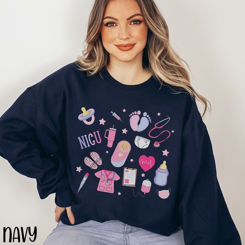 May include: A navy blue sweatshirt with a pink and blue graphic design featuring a variety of baby-related icons, including a pacifier, a syringe, a stethoscope, a baby bottle, and the word "NICU".
