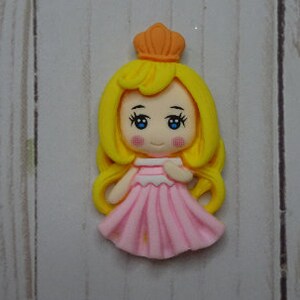 May include: A princess figurine with a yellow crown and long, flowing yellow hair. She wears a pink dress and has blue eyes and rosy cheeks. The figurine is likely made of polymer clay.