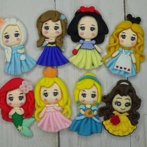 May include: A collection of eight handmade princess figurines. Each figurine is uniquely designed with vibrant colors, featuring detailed dresses, hairstyles, and facial expressions. The figurines are arranged on a light-colored wooden surface.
