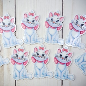 May include: A collection of white cat stickers with blue shading, pink bows, and pink neck ribbons. The stickers feature a cartoon cat with a sweet expression. The stickers are arranged on a light wood grain surface.