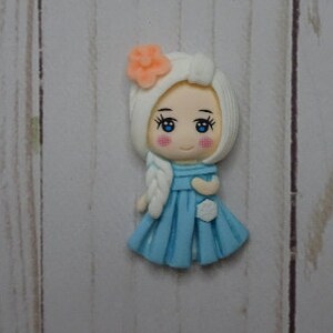 May include: A handcrafted figurine of a cartoon girl with white hair and a blue dress. The figurine has a peach-colored flower in her hair and a white braid. The girl has blue eyes and rosy cheeks. The figurine is on a light wood grain surface.