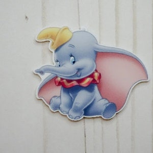 May include: A blue and pink cartoon elephant with a yellow hat. The elephant is sitting down and has a red and yellow collar.