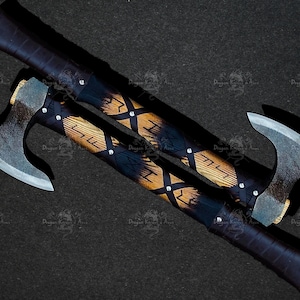 May include: Two Viking axes with black leather wrapped handles and wooden shafts with a brown and black patterned design. The axes have a silver blade and a black leather handle.