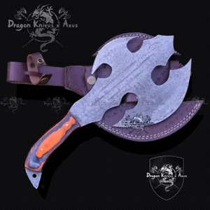 May include: A handmade axe with a leather sheath. The axe has a Damascus steel blade with a triple-pronged head and a wooden handle. The sheath is brown leather with stitching and a belt loop.