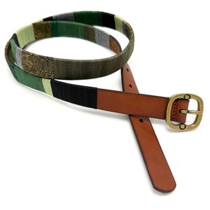 May include: A belt featuring a brown leather strap with a brass-toned buckle and a section wrapped in multicolored thread. The thread pattern includes alternating segments of olive green, black, light green, metallic gold, and silver-toned fibers.