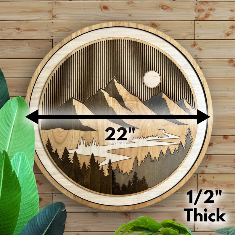 Pode incluir: Uma pe&ccedil;a de arte de parede redonda de madeira com um design de paisagem de montanha. A obra de arte tem 55,88 cm de di&acirc;metro e 1,27 cm de espessura. O design inclui montanhas, &aacute;rvores, um rio e um sol, todos feitos de madeira em camadas.