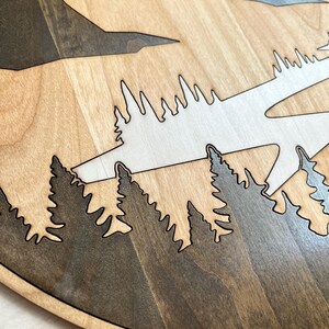 Pode incluir: Cena de montanha e floresta em madeira, cortada a laser a partir de madeira em camadas. O design apresenta montanhas e &aacute;rvores castanhas escuras sobre um fundo castanho claro. As &aacute;rvores s&atilde;o de um tom mais escuro de castanho, com um c&eacute;u castanho claro.
