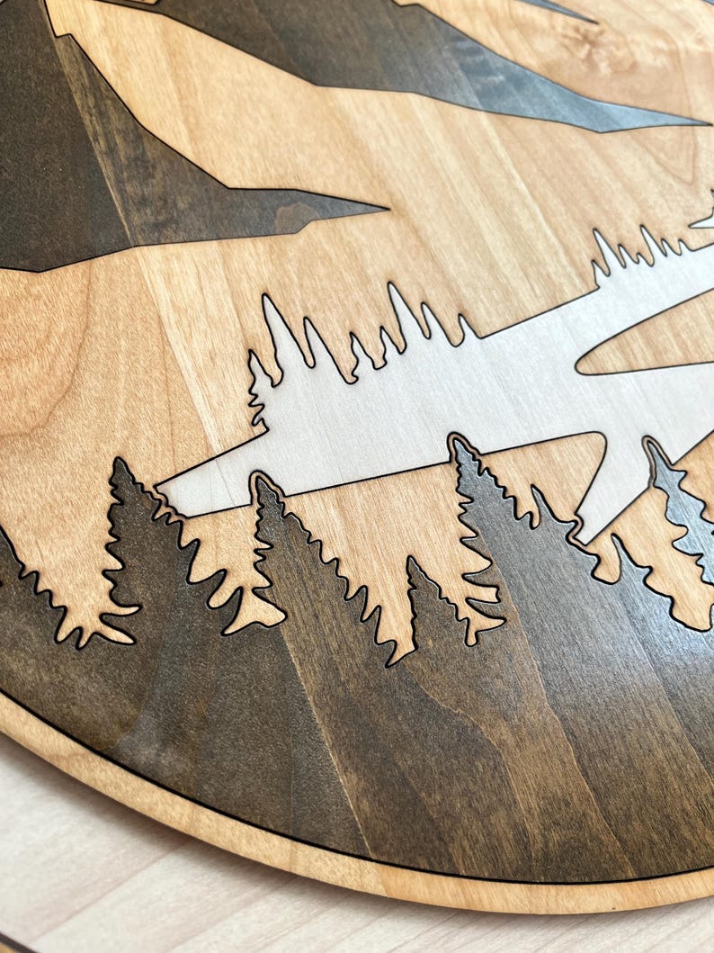 Pode incluir: Cena de montanha e floresta em madeira, cortada a laser a partir de madeira em camadas. O design apresenta montanhas e &aacute;rvores castanhas escuras sobre um fundo castanho claro. As &aacute;rvores s&atilde;o de um tom mais escuro de castanho, com um c&eacute;u castanho claro.