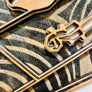 May include: A layered wooden wall art piece featuring a natural light wood finish on the top cutouts and a dark stained wood background with a repeating pattern of curved, wave-like lines. The design includes stylized, abstract human figures.