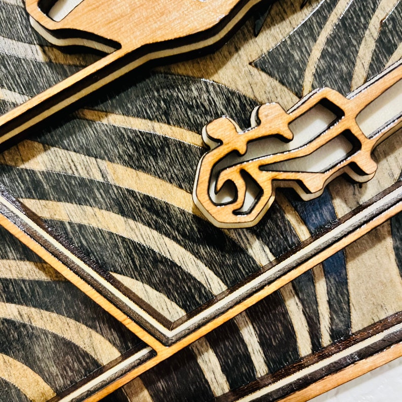 May include: A layered wooden wall art piece featuring a natural light wood finish on the top cutouts and a dark stained wood background with a repeating pattern of curved, wave-like lines. The design includes stylized, abstract human figures.