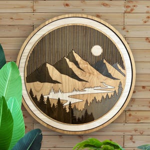 Pode incluir: Uma pe&ccedil;a de arte de parede redonda em madeira com uma paisagem de montanha. O design inclui madeira em camadas com uma cordilheira, um rio, &aacute;rvores e um sol. A pe&ccedil;a tem um acabamento em madeira natural com tons castanhos escuros e claros.