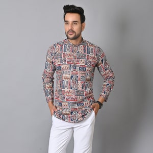 Puede incluir: Una camisa de manga larga estampada en tonos rojos, azules y beige, combinada con pantalones blancos y zapatos marrones. La camisa presenta un diseño geométrico. El atuendo es adecuado para ocasiones informales o semiformales.