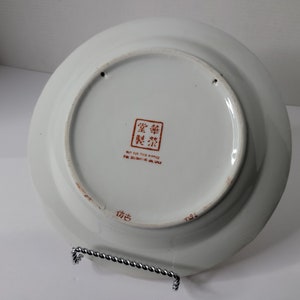 Puede incluir: Plato de cer&aacute;mica blanco con un dise&ntilde;o de caracteres chinos rojos en la parte posterior. El plato dice "No apto para fines alimenticios, solo para uso decorativo".