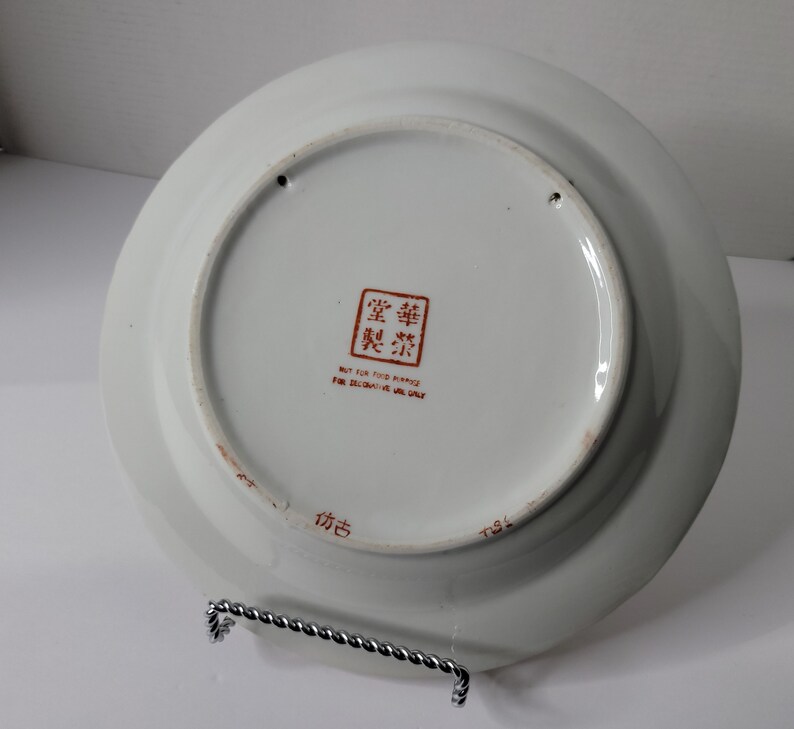 Puede incluir: Plato de cer&aacute;mica blanco con un dise&ntilde;o de caracteres chinos rojos en la parte posterior. El plato dice "No apto para fines alimenticios, solo para uso decorativo".