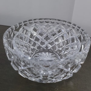 May include: A clear, cut-glass bowl with a diamond pattern. The bowl has a round shape with a scalloped rim and a starburst design on the base. The bowl is sitting on a dark surface.