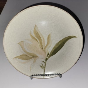 May include: A white ceramic bowl with a green and brown floral design. The bowl has a slightly textured surface and a rounded shape.