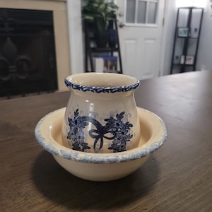 May include: A cream-colored ceramic bowl with a blue floral design. The bowl is nested inside a larger cream-colored ceramic bowl with a blue floral design.