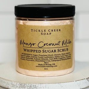 May include: A pink whipped sugar scrub jar with a brown label that reads "Tickle Creek Soap Mango Coconut Milk Whipped Sugar Scrub". The label lists the ingredients and states "Made in Boring, OR" and "www.ticklecreeksoap.com". The jar is 8 oz.